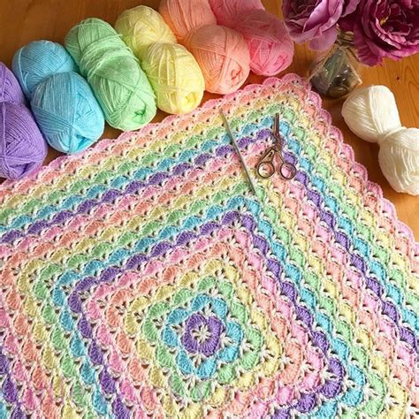 A Crochet Granny Blanket With Yarn And Scissors On The Table Next To It