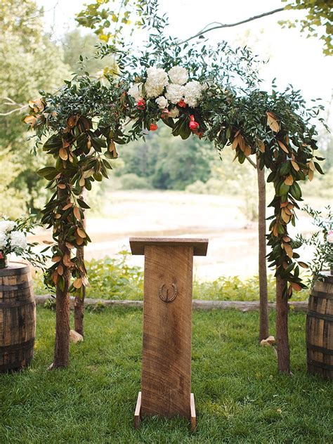An Outdoor Ceremony Setup With Flowers And Greenery On The Arch