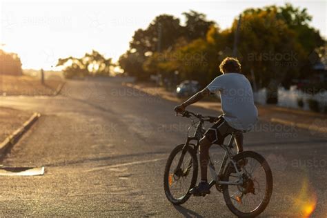 Image Of Teenager Riding Bike With No Helmet On Quiet Evening Street
