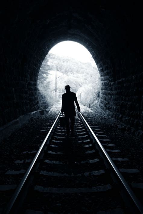 A Man Is Walking Through A Tunnel With Railroad Tracks In The