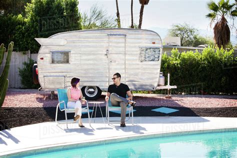 Couple Relaxing By Swimming Pool With Camper Van In Background Stock