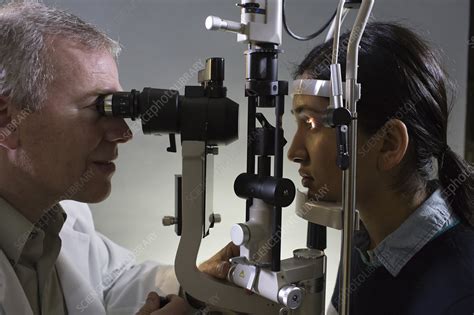 The individual will sit in a chair facing the slit lamp with their chin and forehead resting on a support. Ophthalmologist using slit lamp tanometer - Stock Image - F021/8903 - Science Photo Library