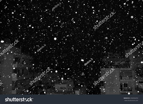 Snow Falling Over City Buildings At Night Black And White