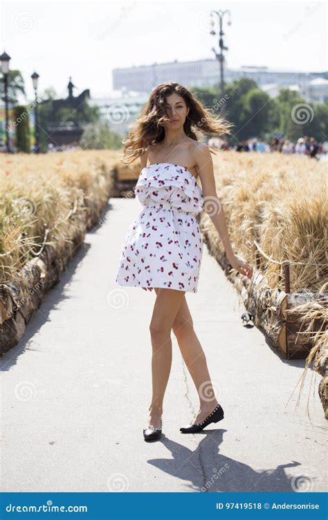 Young Beautiful Brunette Woman In White Dress Walking On The Street