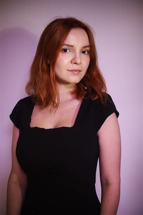 A Woman In A Black Dress Posing For A Photo Against A Purple Background