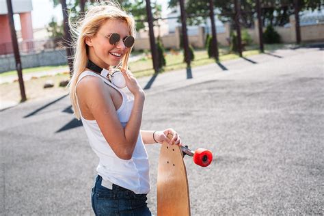 Outdoor Summer Lifestyle Portrait Of Pretty Stylish Blonde Woman Posing With Longboard And