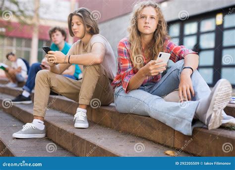 Group Of Teenagers Smartphones Sitting On Stairs In School Campus Stock