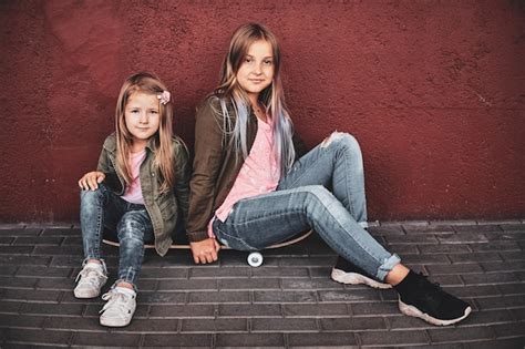 duas meninas bonitas estão relaxando na rua enquanto estão sentadas no skate foto grátis