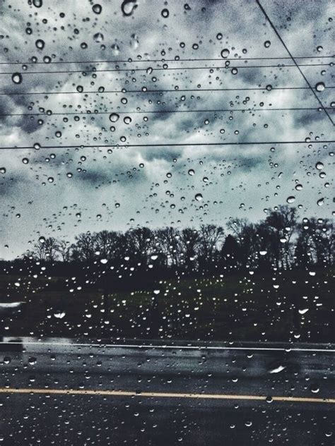 Rain Drops On The Windshield Of A Car As It Drives Down A Road With Power Lines In The Background