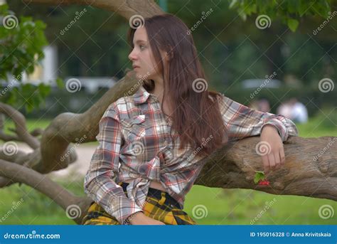 Slender Brunette Girl In A Plaid Skirt And Blouse In The Summer By A