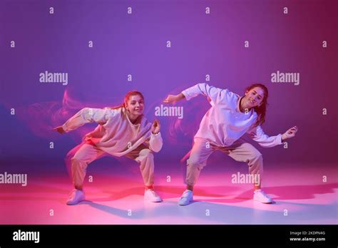 Portrait Of Two Young Girls Dancing Hip Hop Isolated Over Gradient Purple Background In Neon