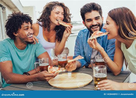 Group Of Young Cheerful People Eating Pizza And Drinking Beer While
