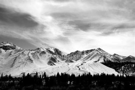 Black And White Image Of A Snow Covered Mountain Range Under A Cloudy