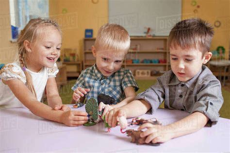 Children Playing With Animal Toys At Table In Classroom Stock Photo