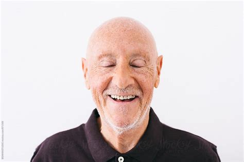 Portrait Of An Elderly Man Laughing With Eyes Closed Over White By Stocksy Contributor