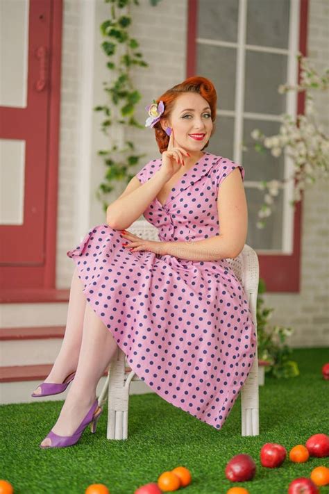 Beautiful Redheaded Pin Up Girl In Pink Polka Dot Dress And Vintage Stockings Posing Near The