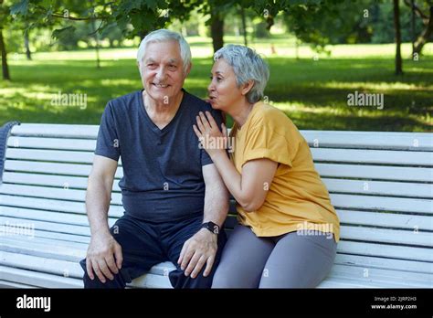 Attractive Older Couple Talking Seated On Bench In Summer Park Wear