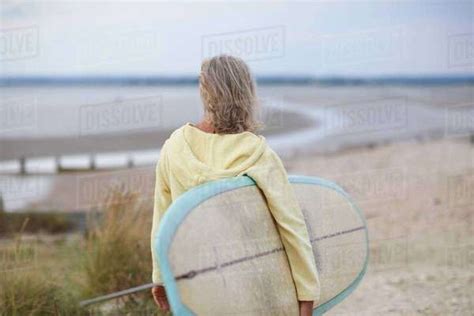 Senior Woman Walking Towards Beach Carrying Surfboard Rear View Stock Photo Dissolve