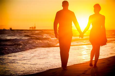 Diverse Couple Walking On Beach At Sunset Stock Photo