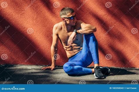 Shirtless Young Athlete Man Sitting Down Wearing Black Sunglasses Looking At One Side Resting