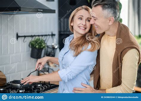 A Couple Hugging In The Kitchen And Looking Happy Stock Photo Image