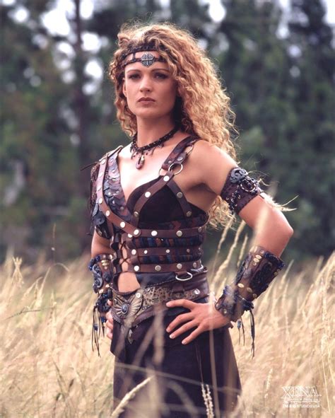a woman with long hair and leather outfit standing in tall grass