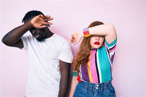 Interracial Couple Wearing Casual Clothes Covering Eyes With Arm Looking Serious And Sad Stock