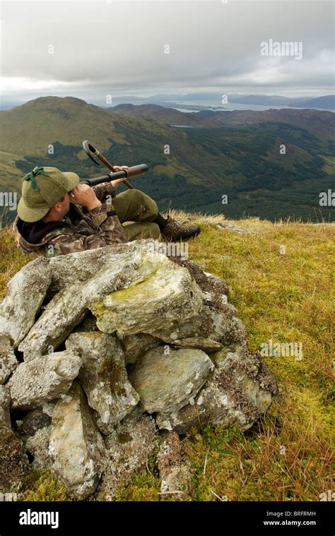 Scottish Deer Stalker On Top Of A Mountain Spying For Deer Using A