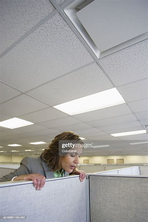 Female Office Worker Peering Over Partition Into Office Cubicle Stock