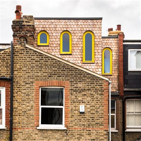 A Loft Extension Featuring Wooden Shingles And Yellow Arched Windows