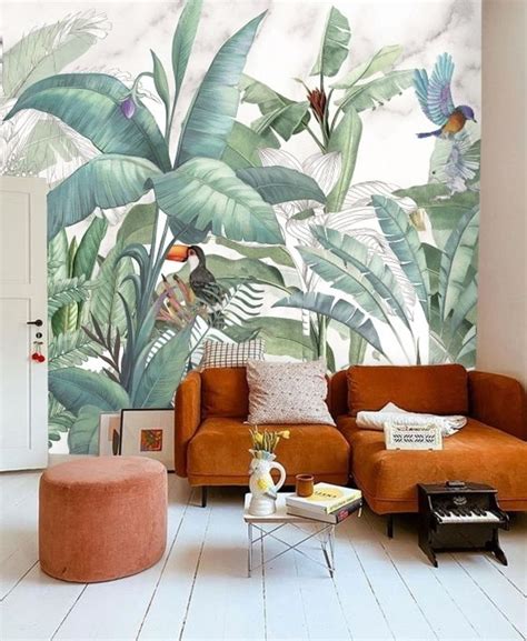 An Orange Couch Sitting In Front Of A Wall Mural With Tropical Leaves