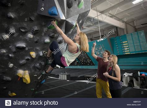 Rock Climbers Watching Woman Climbing Wall In Climbing Gym Stock Photo