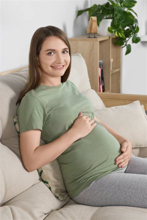 happy pregnant woman sitting on sofa and touching her belly in living room stock image image