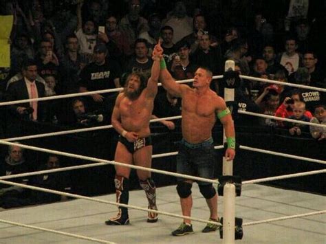 Two Men Standing Next To Each Other In A Wrestling Ring Holding Their Hands Up While People