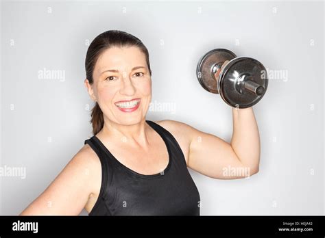 Middle Aged Woman In A Black Sports Top Lifting Heavy Dumbbell Smiling Happy And Proud Light