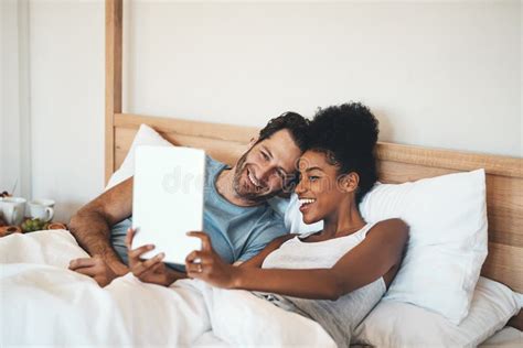 Happy Couple Taking Selfie On A Tablet In Bed Together After Waking Up Interracial Husband And