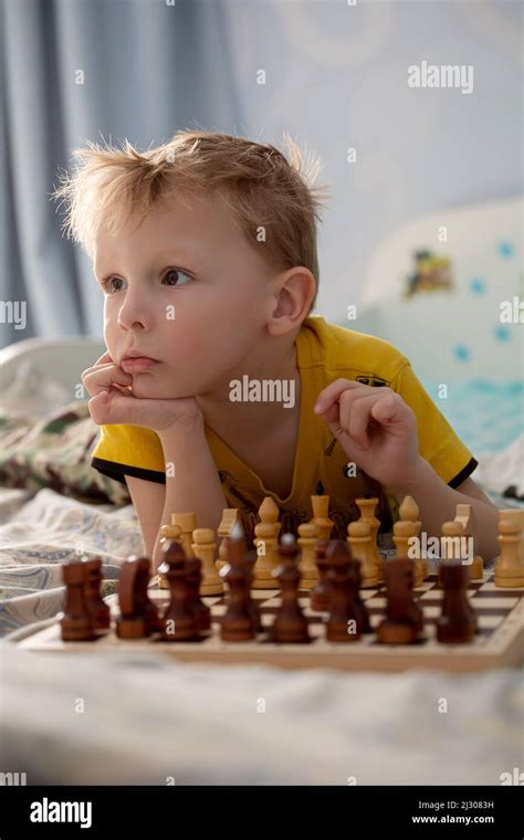 A Little Boy Lying On The Bed In Front Of A Chess Board Is Playing