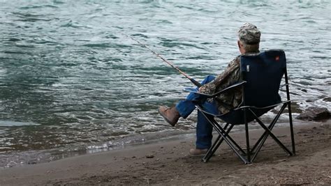 Man Sitting In A Folding Chair On The Bank Of A Large River In Alaska