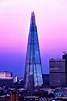 the shardle building is lit up in blue and pink colors, with other tall ...