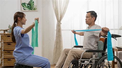 Side View Of Asian Disable Mature Man Sitting In Wheelchair And Working Out With Female Personal