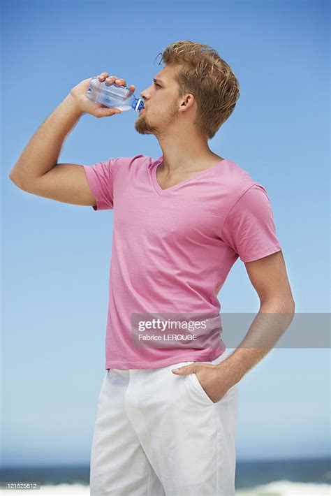 Young Man Drinking Water From A Water Bottle On The Beach High Res