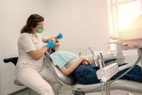 Female Dentist Treats The Teeth Of A Young Girl Patient Lying In The