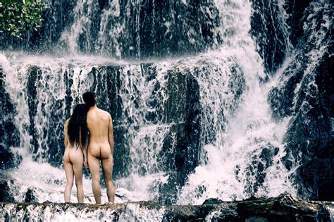 Back View Of Nude Couple Standing Close To Each Other And Enjoying Scenery Of Waterfall In