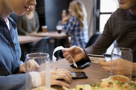 Some issuers specifically offer rewards on food delivery, but not all do. Close up couple with credit card paying bill calculating tip with smart phone in brewery ...