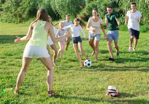 Two Friendly Families With Children Playing Football In Nature At