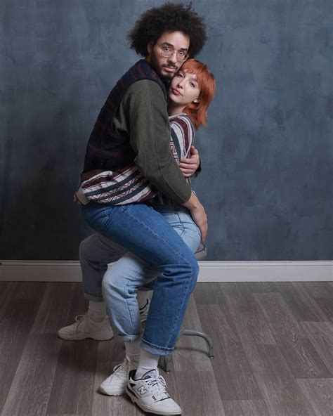 A Man And Woman Hug Each Other While Sitting On A Chair In Front Of A Wall