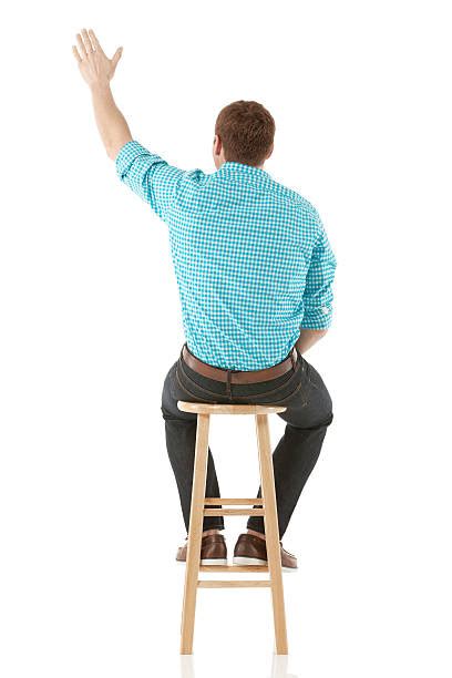 Rear View Of Man Sitting On Stool With Hand Raised Stock Photos