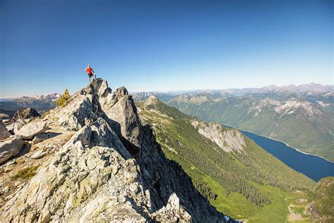 Hiker Standing On Mountain Summit With View Of Lake And Forest Below