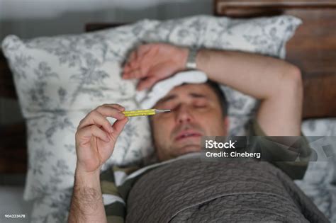 Sick And Tired Man Lying In Bed Checking His Temperature Stock Photo
