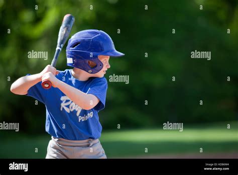 Boy Hitting Ball Whilst Playing Baseball In A Blue Uniform Stock Photo